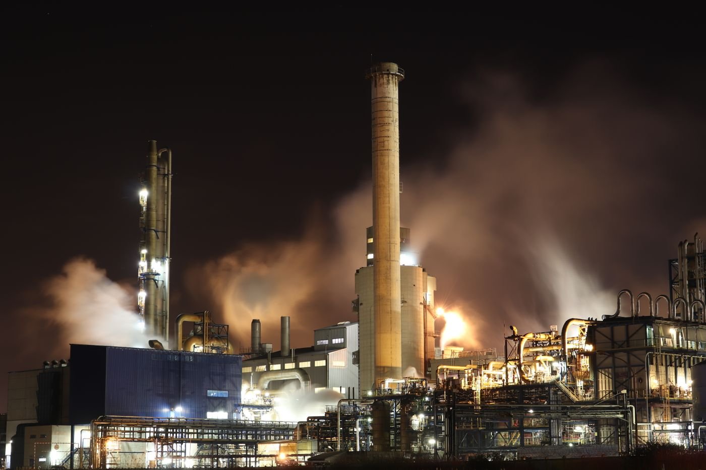 Industrial plant with process piping and stack lit up at night.